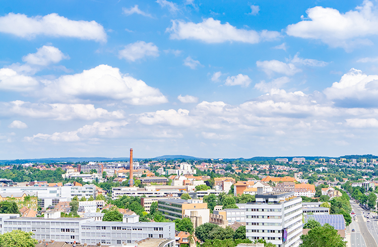 A vibrant city with a clear, sunny sky, featuring diverse tall buildings, streets lined with trees in residential areas