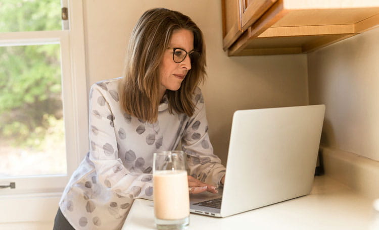 Woman working on laptop in kitchen with glass of milk