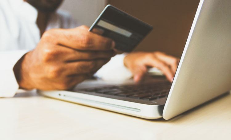 man holding bank card in front of laptop