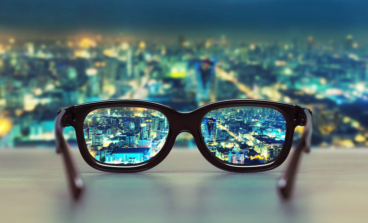 glasses on desk inside skyscraper office looking out at night time city
