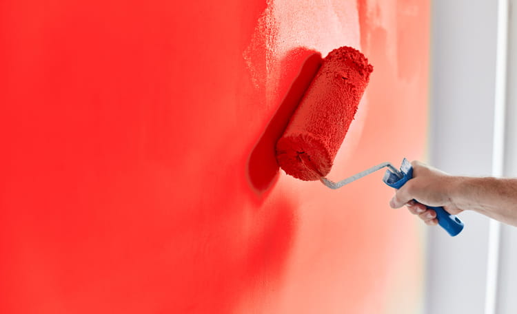 person painting wall red with a roller brush